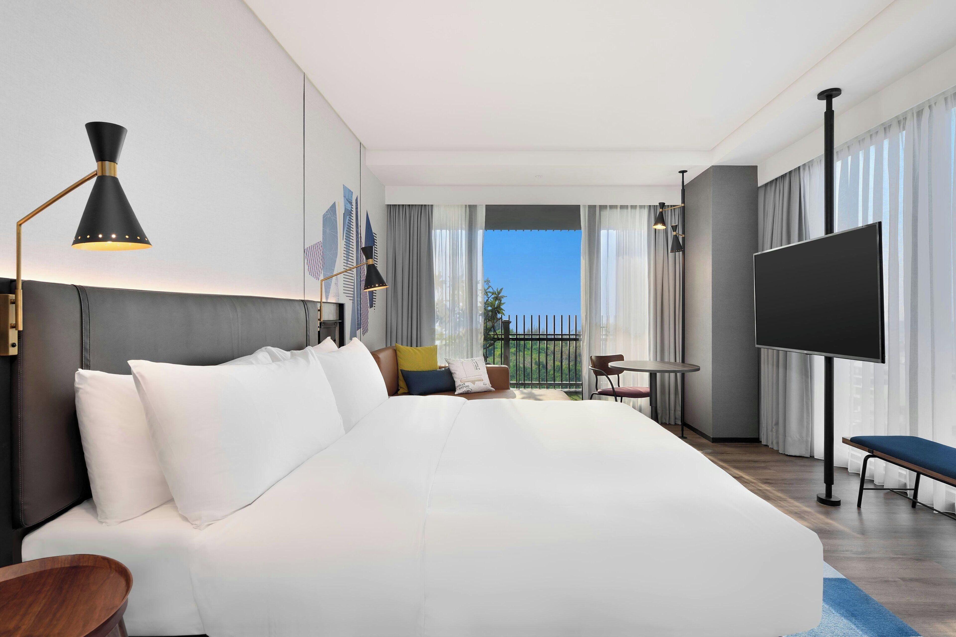 Una habitación de hotel moderna con una cama grande, televisión, escritorio y balcón con vistas.