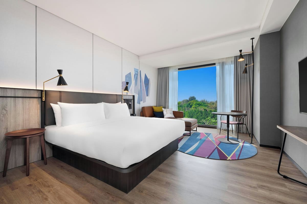 Quarto de hotel moderno com uma cama grande, uma escrivaninha, uma cadeira e vista para o exterior.