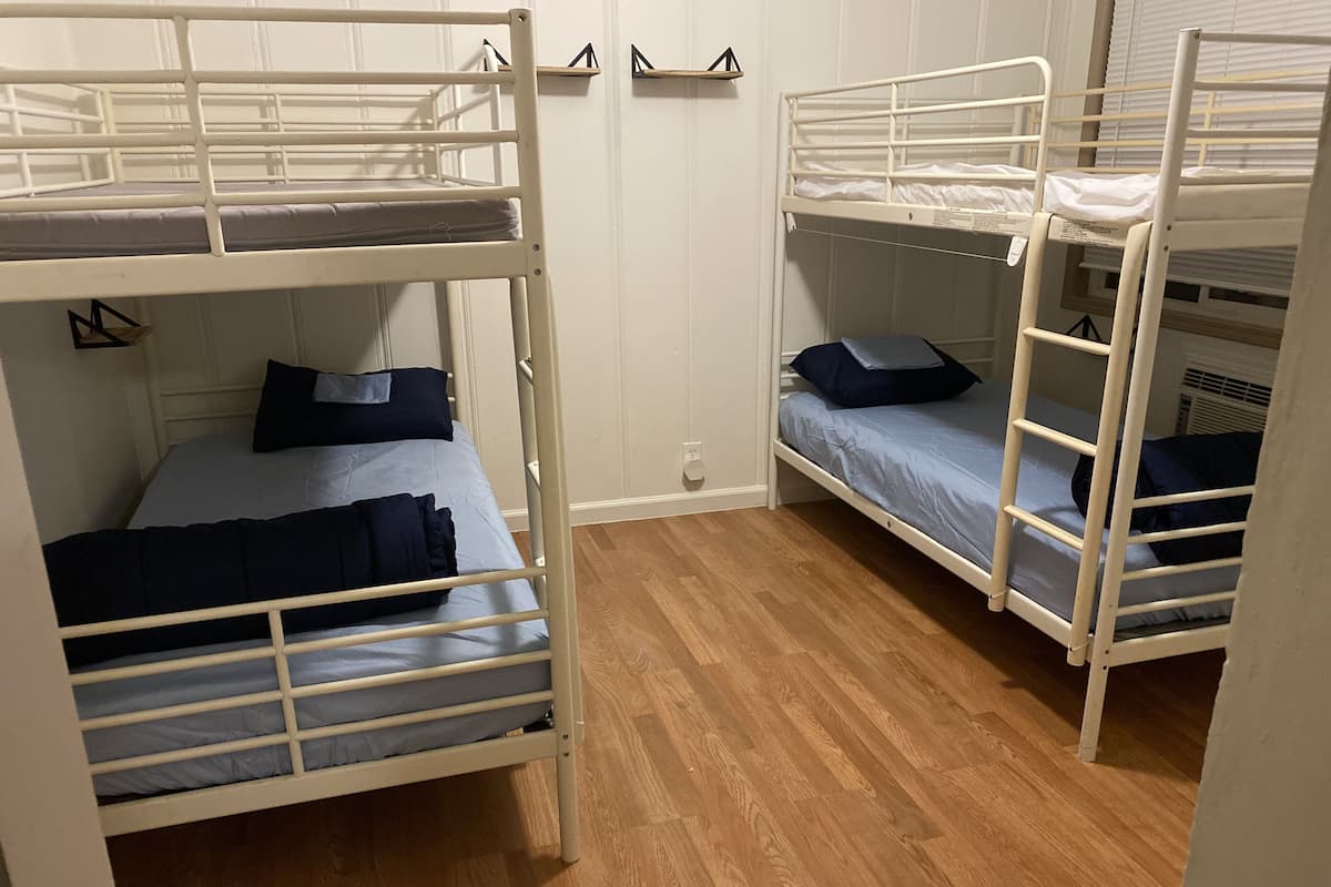 A room with two bunk beds, wooden flooring, and white walls.