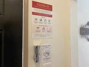 A door with a COVID-19 safety policy sign and a hand sanitizer dispenser. - WHOLE Family - Barrette - Hostel (Sacramento)