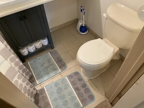 A bathroom with a toilet, a shelf with toilet paper, and two mats on the floor. - WHOLE Family - Barrette - Hostel (Sacramento)