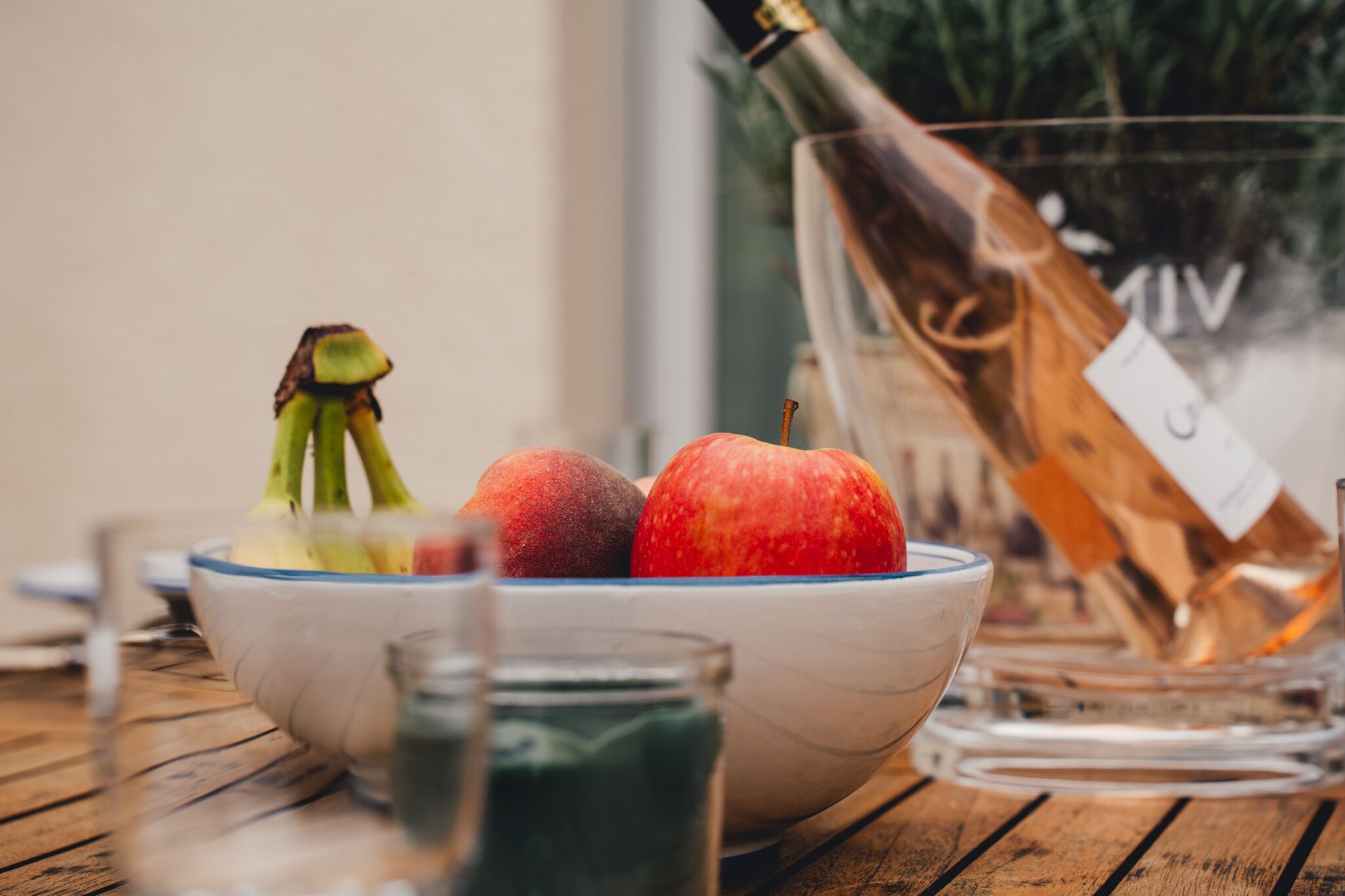 A wooden table with a bowl containing two apples and a bottle of champagne.