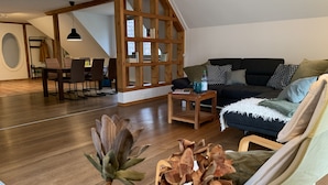 A spacious loft with a dining area, a built-in wooden bookshelf, a cozy seating area with a sofa and armchairs, and a dining table with chairs. - Varus vacation apartment in the Kalkriese recreation area surrounded by meadows and forests (Ostercappeln)