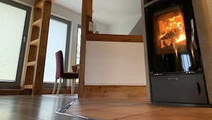 A room with a wood-burning stove, wooden beams, a chair, and a window. - Varus vacation apartment in the Kalkriese recreation area surrounded by meadows and forests (Ostercappeln)