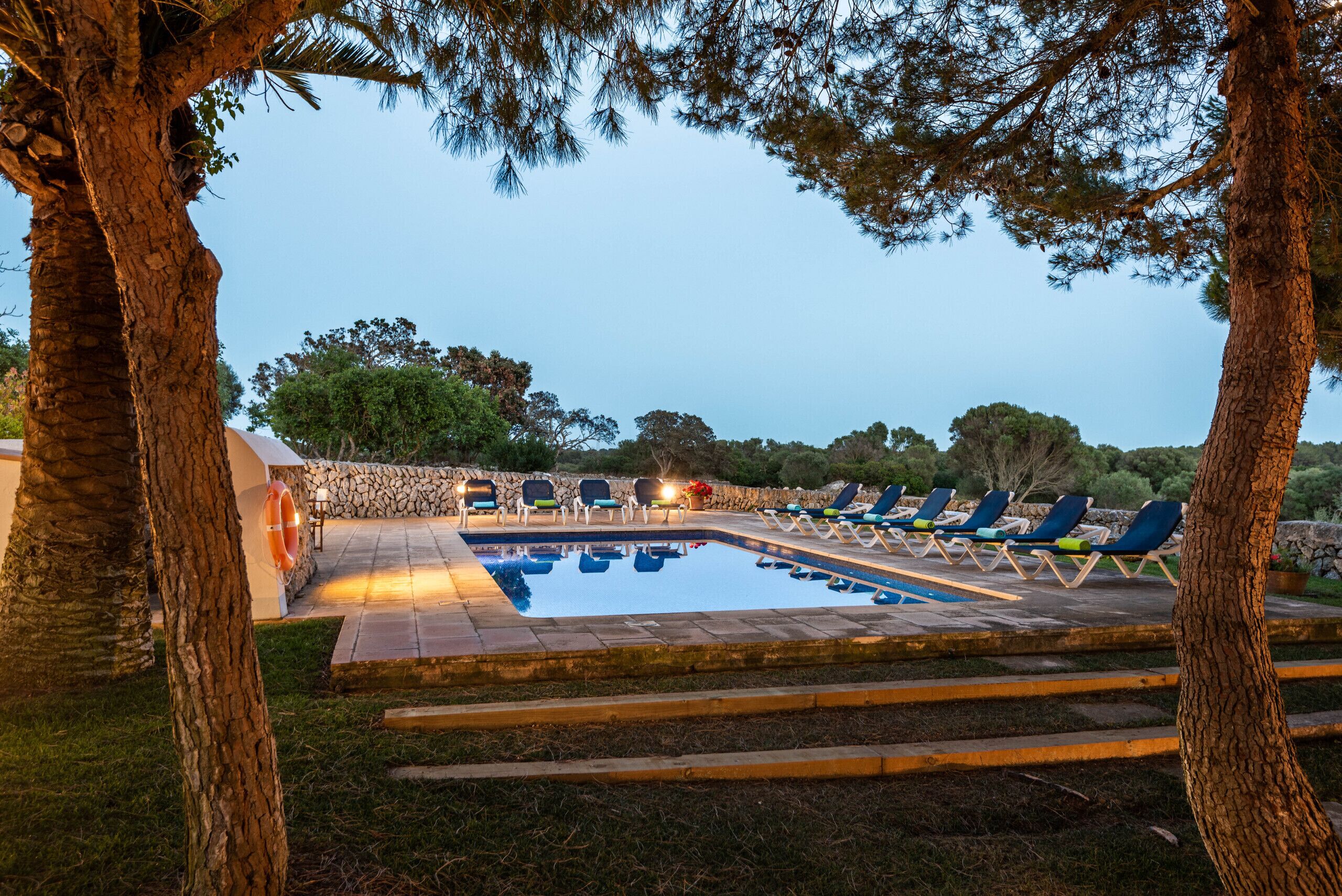 A swimming pool with lounge chairs and a stone wall in the background.