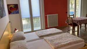 Un dormitorio con cama, un radiador, una mesa con sillas y un balcón.