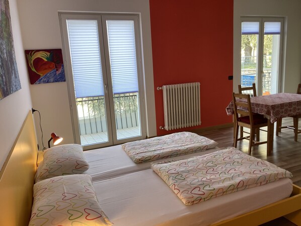 A bedroom with a bed, a radiator, a table with chairs, and a balcony.