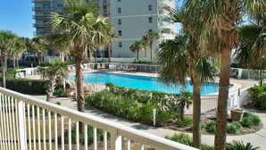 A hotel with a swimming pool surrounded by palm trees and a white fence. - Gulf Front Condo, outdoor/ indoor pools, Large wrap around balcony, 3br/2ba (Orange Beach)