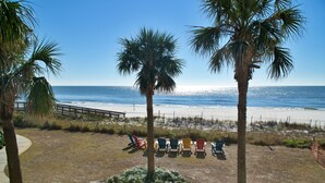 A beach view with palm trees, a sandy area with colorful Adirondack chairs, and a clear blue sky. - Gulf Front Condo, outdoor/ indoor pools, Large wrap around balcony, 3br/2ba (Orange Beach)