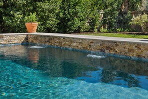 Piscina cristalina con borde de piedra y valla de madera al fondo.