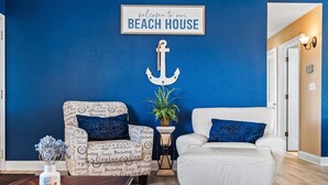 Een woonkamer met een blauwe wand, een witte bank, een gestreept fauteuil, en een bordje met de tekst 