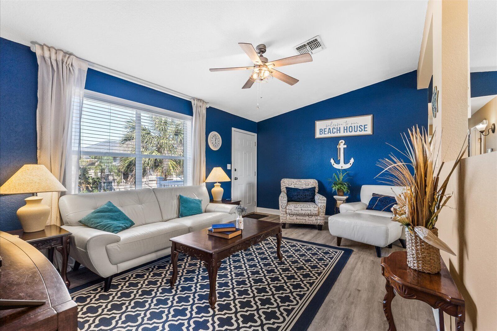 A living room with a blue and white color scheme, featuring a white sofa, a wooden coffee table, and a patterned rug.