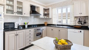 Cucina con mobili bianchi, forno a microonde, forno e lavastoviglie. Sul piano di lavoro c'è un cesto con limoni.