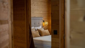 A wooden room with a bed, a wall-mounted lamp, and a wooden door. - Les Jardins du Herisson 4 (BONLIEU)