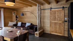 A cozy wooden interior with a dining area, leather sofas, a wooden door, and a hanging light fixture. - Les Jardins du Herisson 4 (BONLIEU)