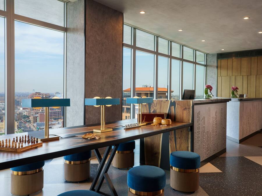 Een moderne hotel lobby met een groot raam met uitzicht op de stad, een receptiebalie en een schaakbord op de tafel.