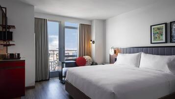 A hotel room with a large bed, a desk with a computer, a chair, and a view of the city through the window.