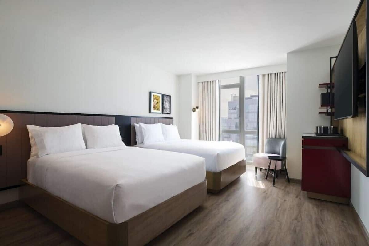 Habitación de hotel con dos camas, un escritorio, una silla, un televisor y una ventana con cortinas.