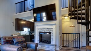 Amplia sala de estar con chimenea, televisor montado y una escalera que conduce a un nivel superior.