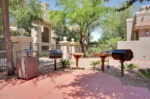 An outdoor patio area with a barbecue grill, trash bins, and a table.