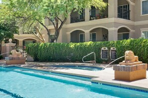 A pool area with a statue, a hedge, and a building with balconies.