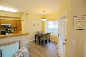 A compact kitchen with a microwave, stove, and dining area with patterned chairs.