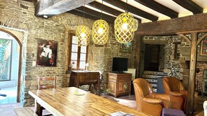 Un interior rústico con una mesa de madera, sillas de cuero, paredes de piedra y lámparas de mimbre colgantes.