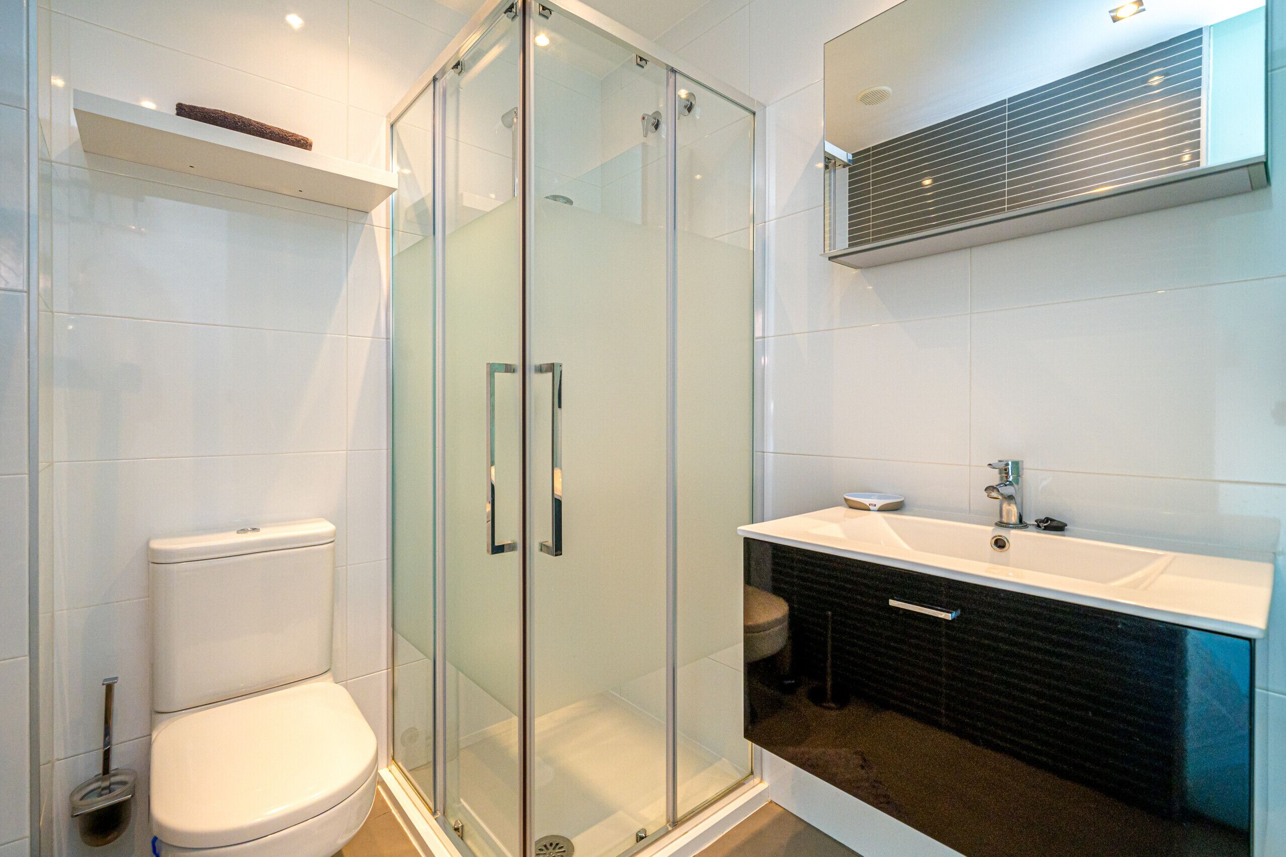 A modern bathroom with a glass-enclosed shower, a white toilet, and a black vanity with a sink.
