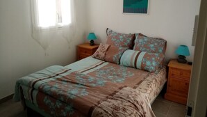Ein Schlafzimmer mit einem Bett, zwei Nachttischen, einem Fenster mit Vorhängen und einem an der Wand hängenden Poster.