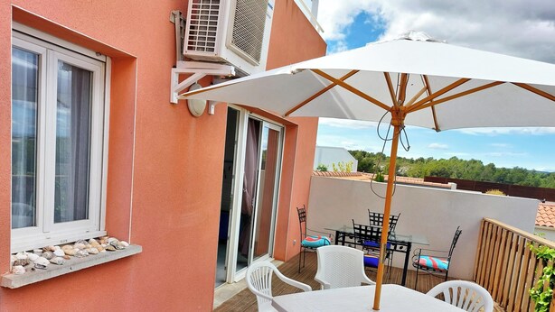 Eine Terrasse mit Tisch und Stühlen, einem weißen Sonnenschirm und einem Fenster mit Muscheln.