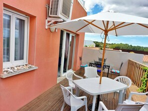 Un patio con una mesa, sillas, un parasol blanco y una ventana decorada con conchas.