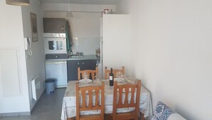 Eine kompakte Küche mit Mikrowelle, Backofen und Spüle. Ein Esstisch mit Stühlen und ein kleiner Mülleimer sind vorhanden.