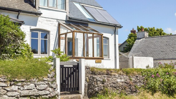 A two-story house with a stone wall entrance, a conservatory, and a clear blue sky.