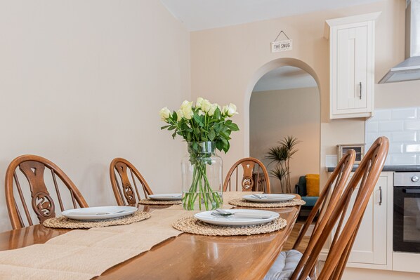 Un coin repas avec une table en bois dressée pour quatre personnes, entourée de chaises, et un vase de fleurs placé au centre.
