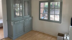 A room with a large window, a built-in cabinet, and a wooden floor.