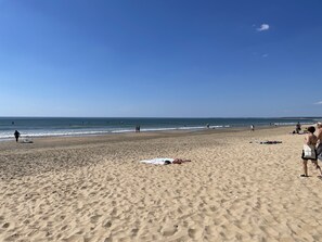 Una playa con gente caminando y parada, y algunos sombrillas en la arena.