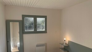 A bedroom with a bed, a window with a view, a bedside table with a lamp, and a radiator.