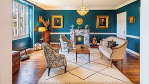 Un salon avec une cheminée, des fauteuils à motifs, un canapé et un lustre.