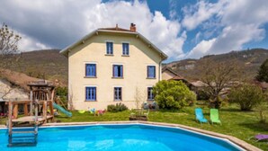 Une maison à deux étages avec une piscine, un toboggan et une pelouse équipée de chaises.