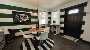 A dining area with a striped wall, a round table with chairs, a hanging light fixture, and a framed artwork.