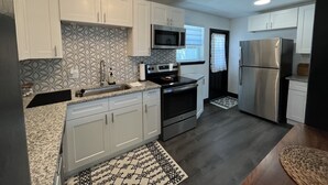 A modern kitchen with white cabinets, a stainless steel refrigerator, a microwave, and a stove.