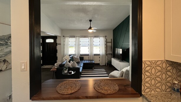 A modern living room with a dark wooden floor, a large window with curtains, a sofa, a coffee table, and a TV.