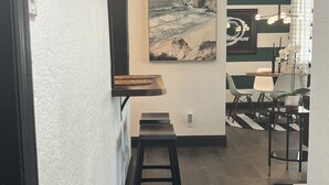 A modern kitchen with a wooden countertop, a stool, and a dining area with chairs and a table.