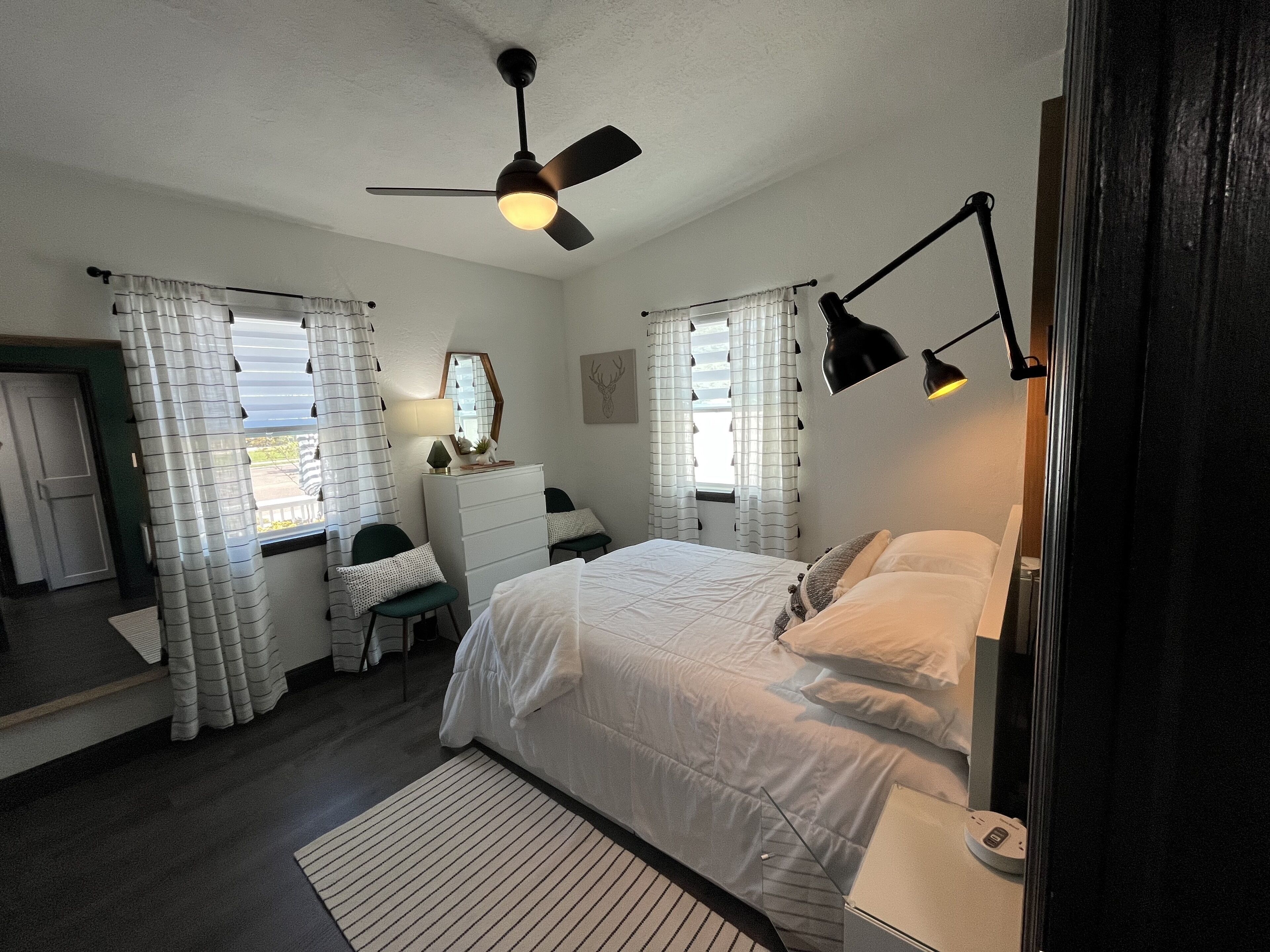 Ein Schlafzimmer mit Bett, Schminktisch, Schreibtisch, Stuhl, Spiegel und Deckenventilator.