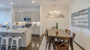 Une cuisine moderne avec un îlot central, un coin repas avec une table et des chaises en bois, et un panneau mural portant l’inscription « Nashville ».