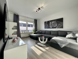 Una sala de estar moderna con un sofá gris, un televisor de pantalla plana y una obra de arte con estampado de tigre.