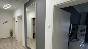 A modern interior with a hallway leading to a room with a large mirror and a small seating area.