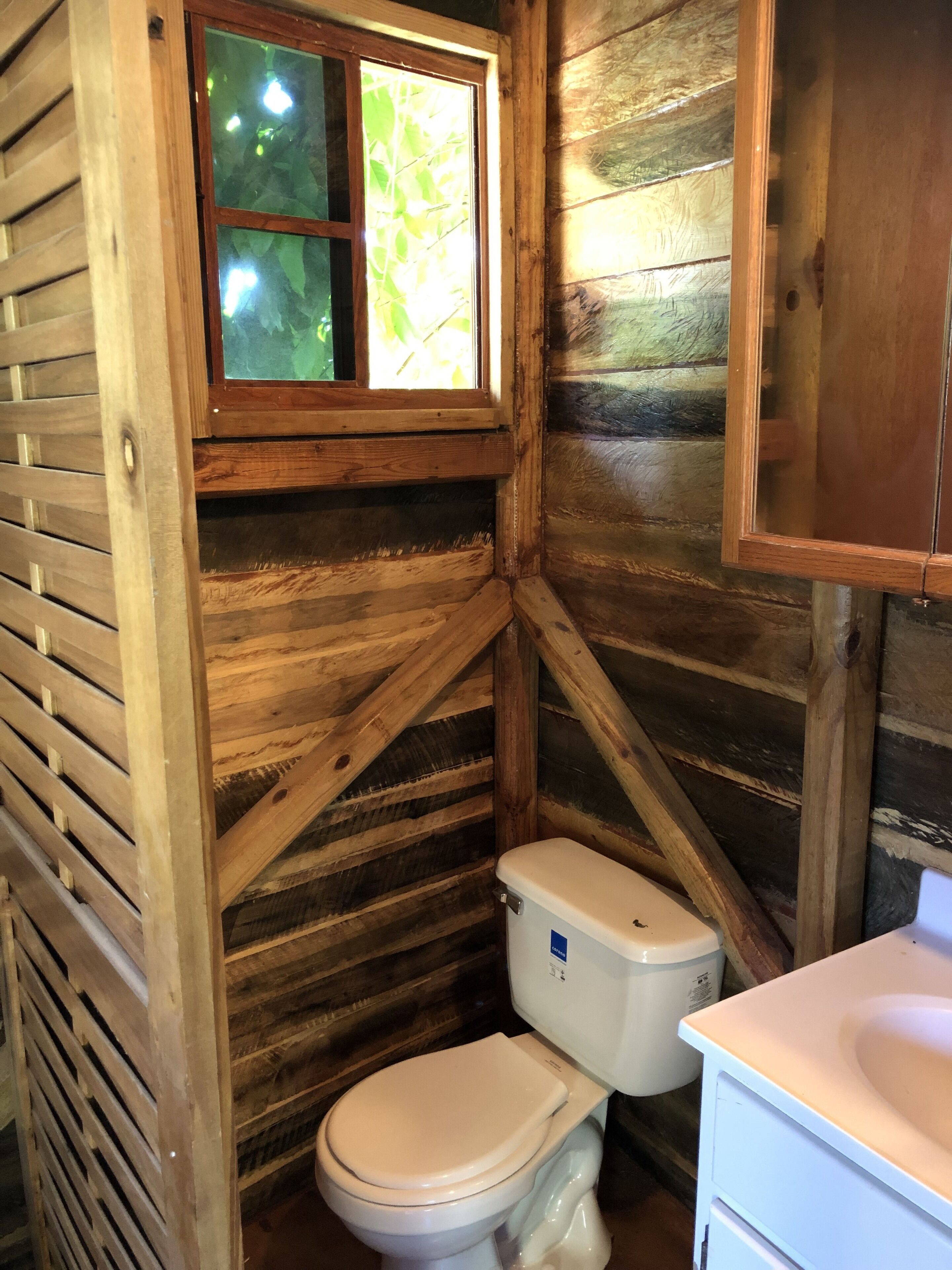 A wooden cabin bathroom with a window, a toilet, and a sink.
