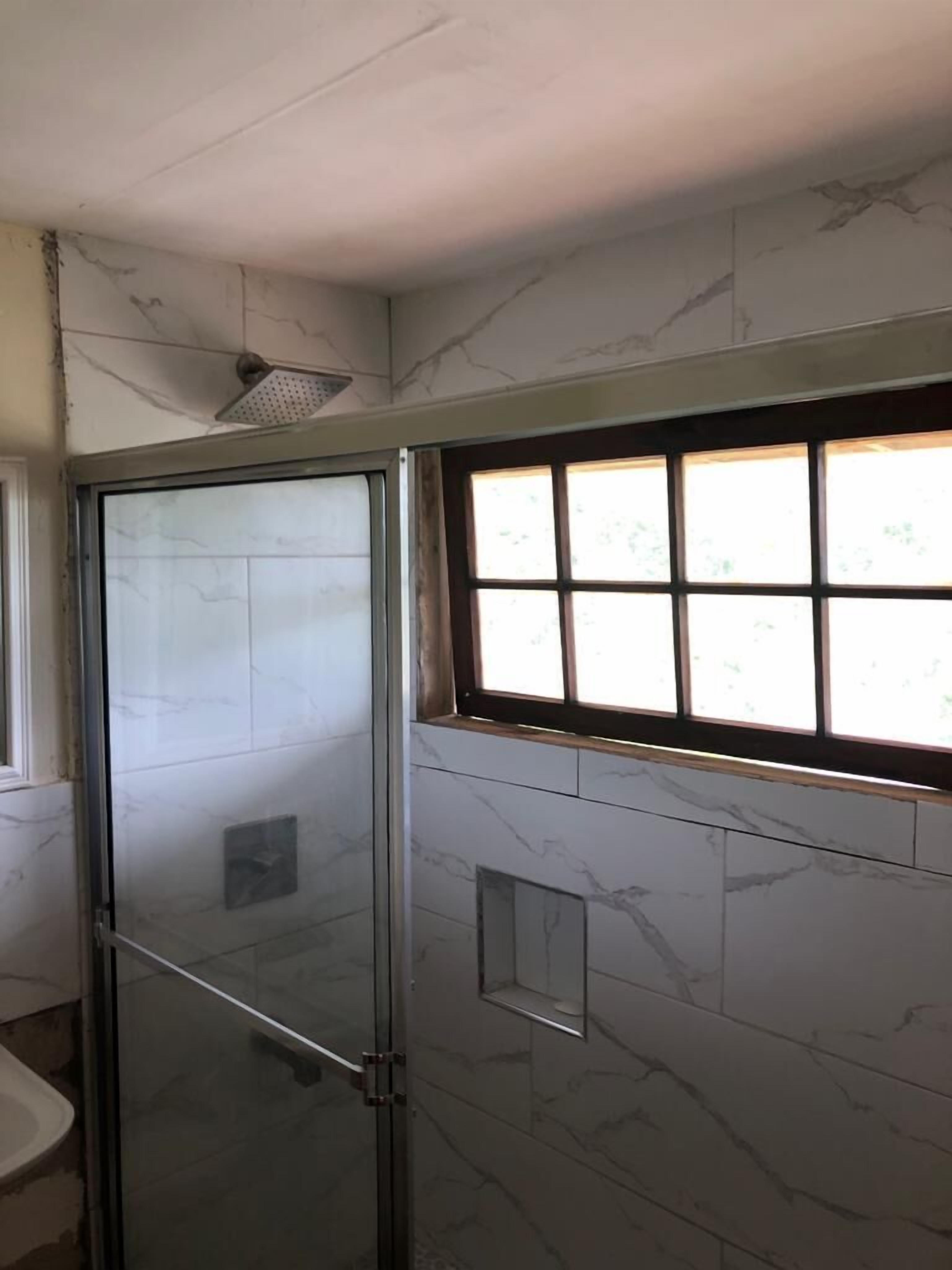 Casa de banho com cabine de duche em vidro, paredes em mármore e janela com vários painéis.