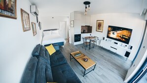 Un saló modern amb un sofà, una taula de centre i una televisió. Hi ha una zona de cuina amb una taula de dinar i cadires.